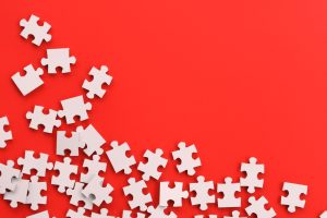 White jigsaw puzzle pieces scattered on red background, copy space, text overlay